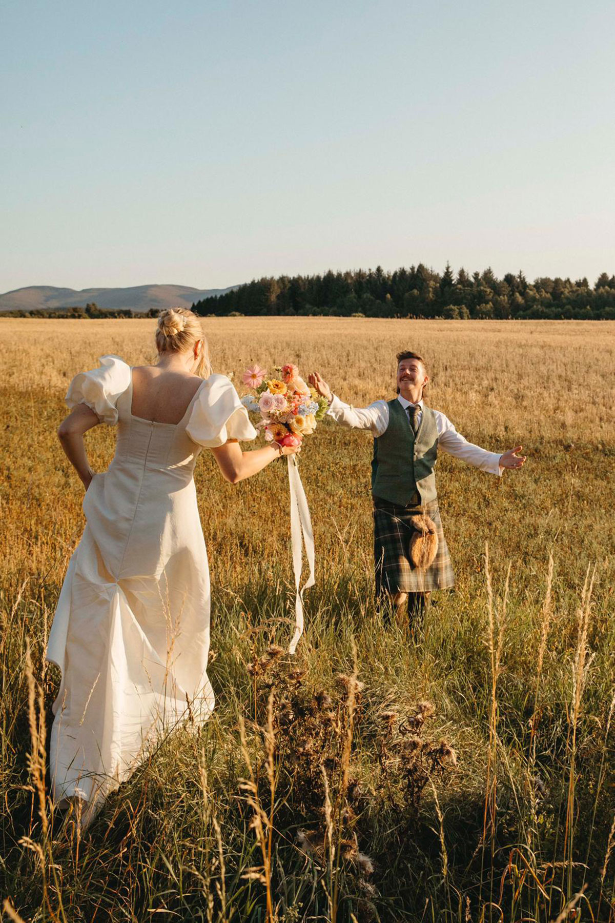 Bride and groom walk hand in hand through Highland field during Cairngorms outdoor wedding portraits