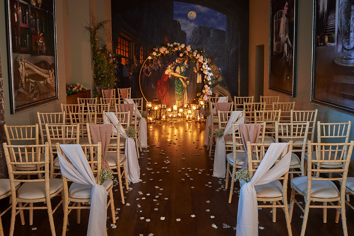 Wedding ceremony setup with candle-lined aisle, floral arch and wooden chairs in an indoor venue