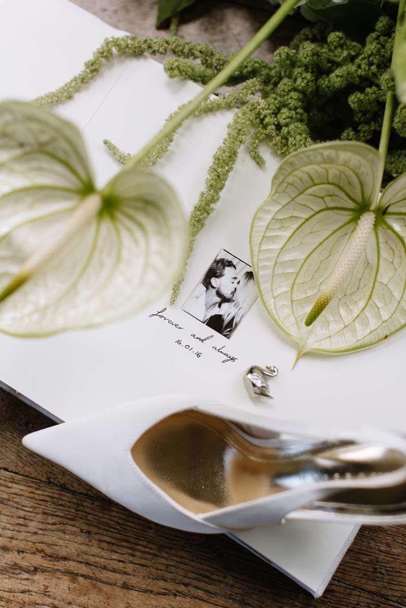 Cambo House wedding details featuring white anthurium flowers, a guest book with a photo of Lia and Louis and a silver swan favour