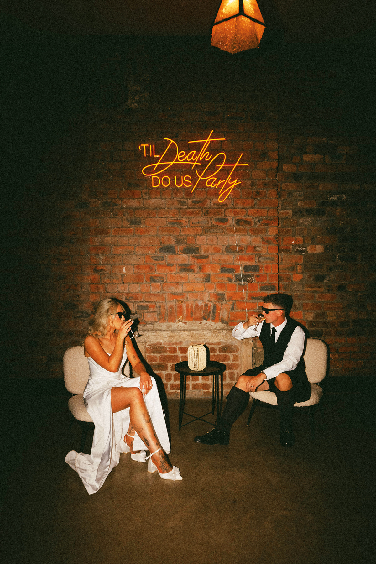 Bride and groom sit beneath a Til Death Do Us Party neon sign at The Engine Works Glasgow