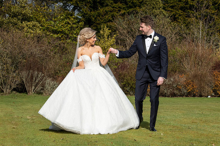 A Bride And Groom Holding Hands Walking On Grass