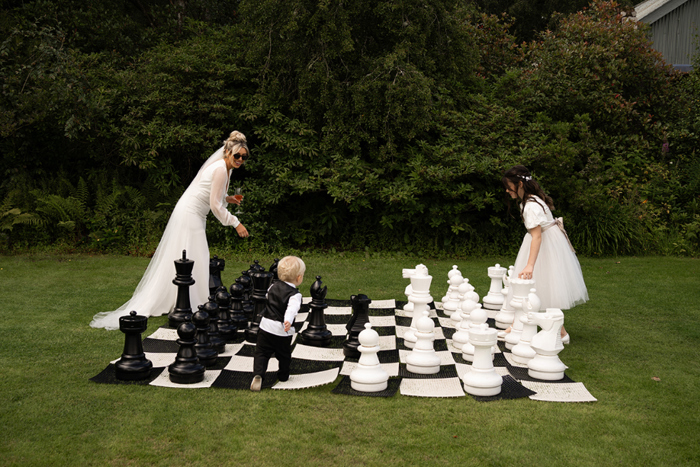 Bride and children Playing Giant Chess Set In Garden