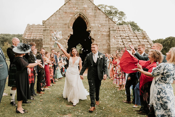 a cheering bride and groom Matt Fagerson walking through two rows of wedding guests throwing confetti outside Dunglass Collegiate Church