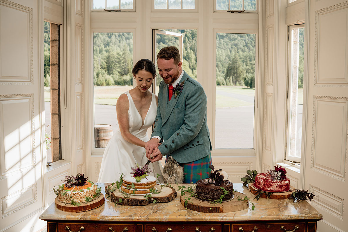 Bride and groom cutting their wedding cake in a light-filled room at Mar Lodge Estate in the Scottish Highlands