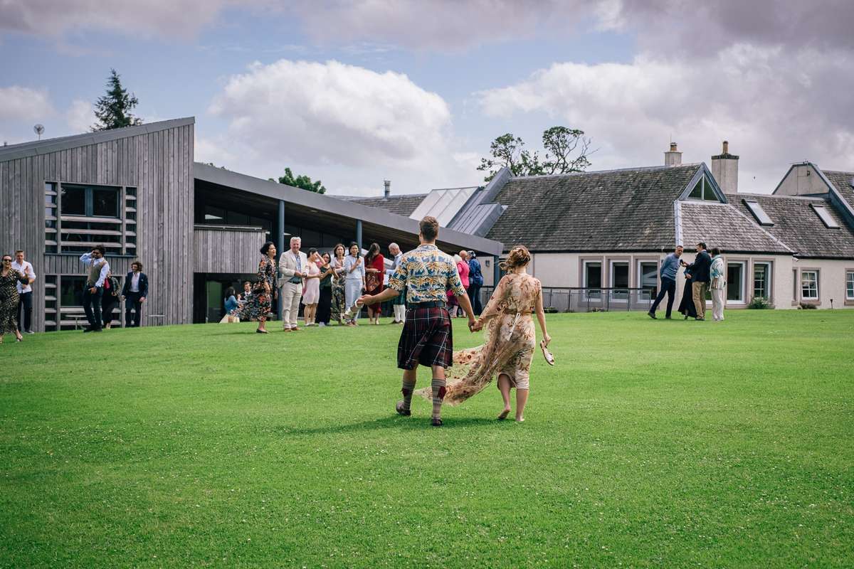 Newlyweds walking across the lawn towards their wedding guests at Ardoch Loch Lomond