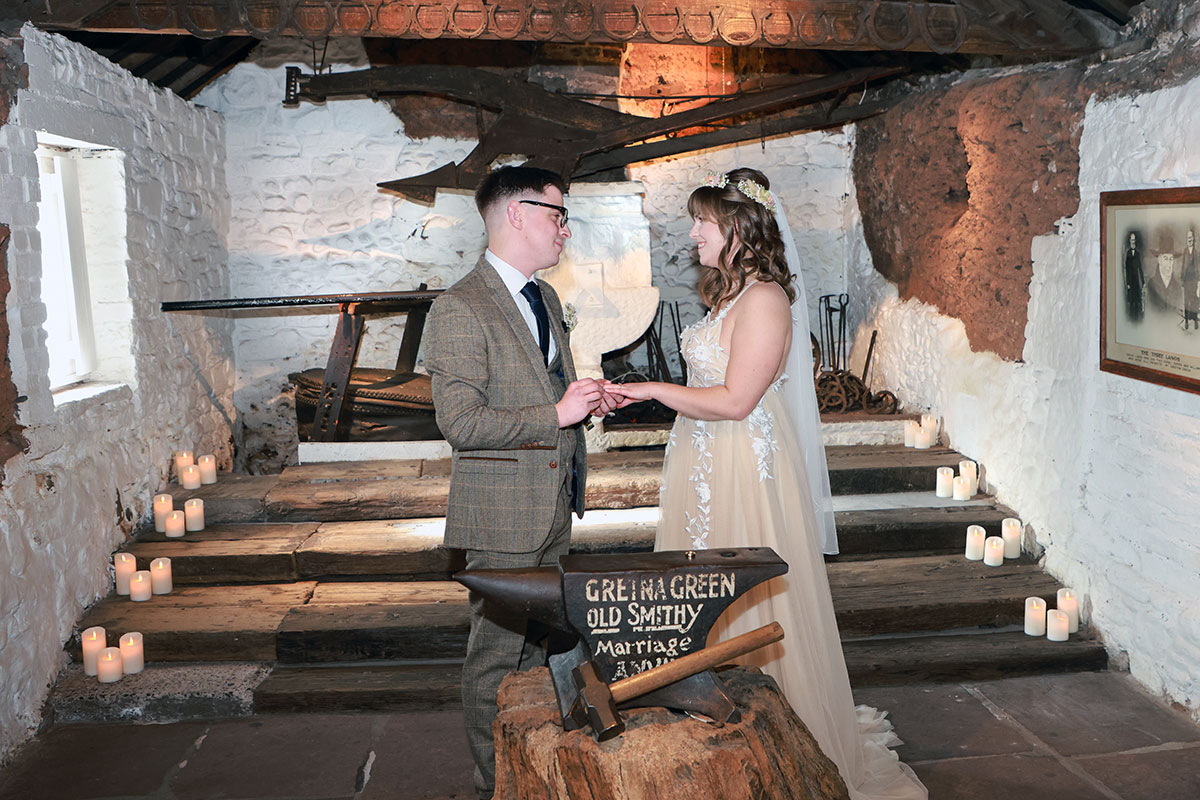 groom places wedding ring on bride's finger during ceremony at gretna green