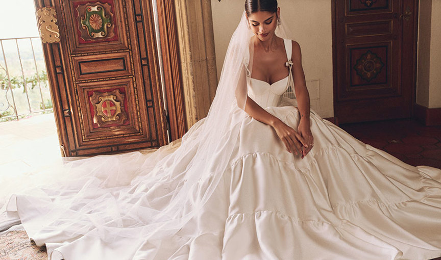 a person sitting down in a Sottero and Midgeley wedding dress with open ornate panelled wooden door in background