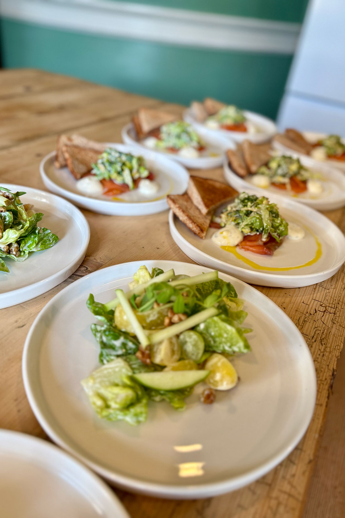 Plated wedding starters laid out on a wooden table, featuring fresh salads and smoked salmon with toast