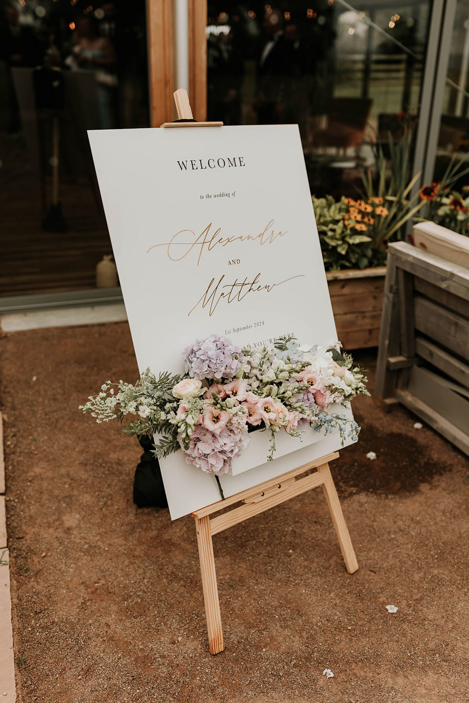 a wedding welcome sign with fresh flowers on easel