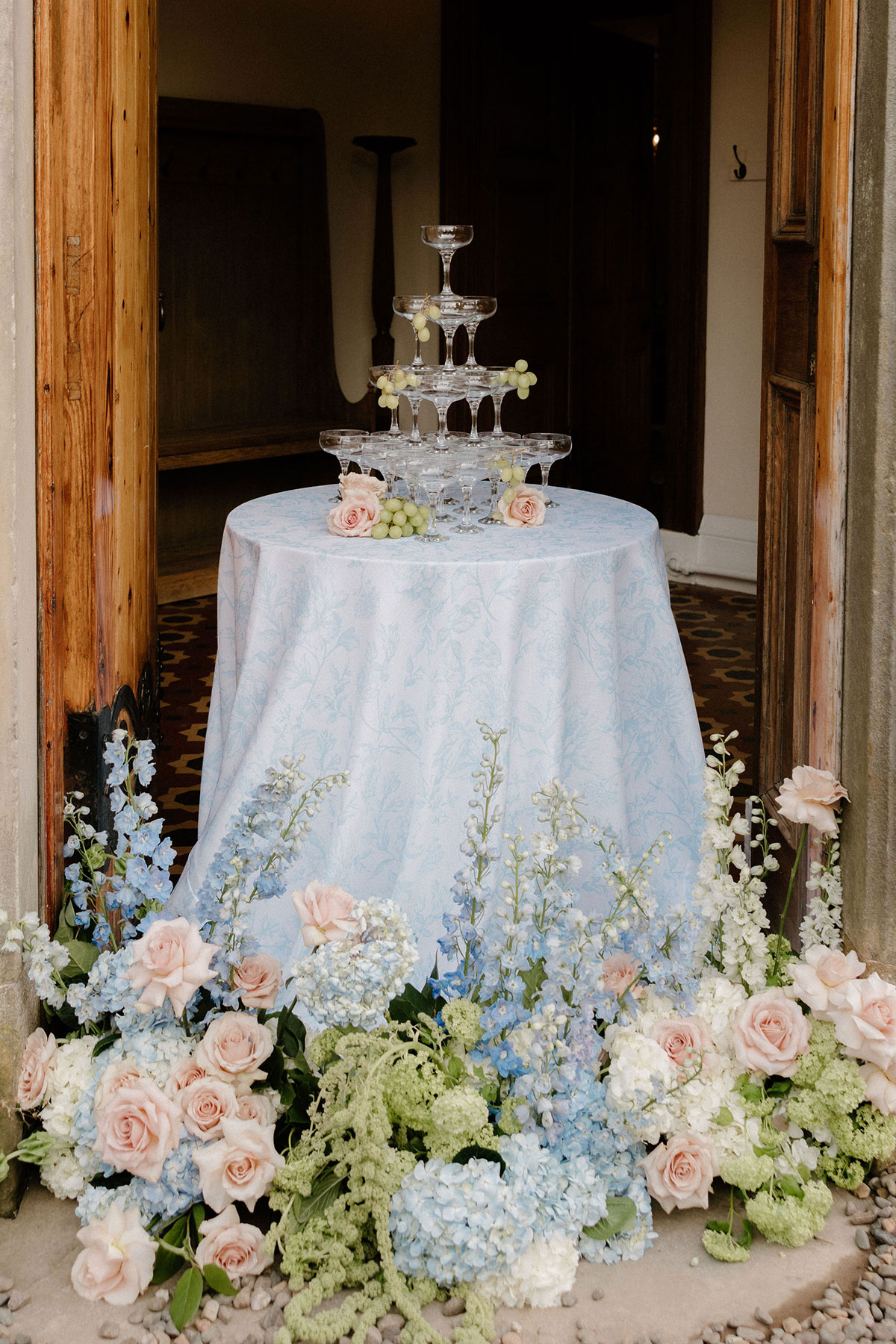 Champagne tower displayed on a blue patterned tablecloth framed by pastel floral arrangements