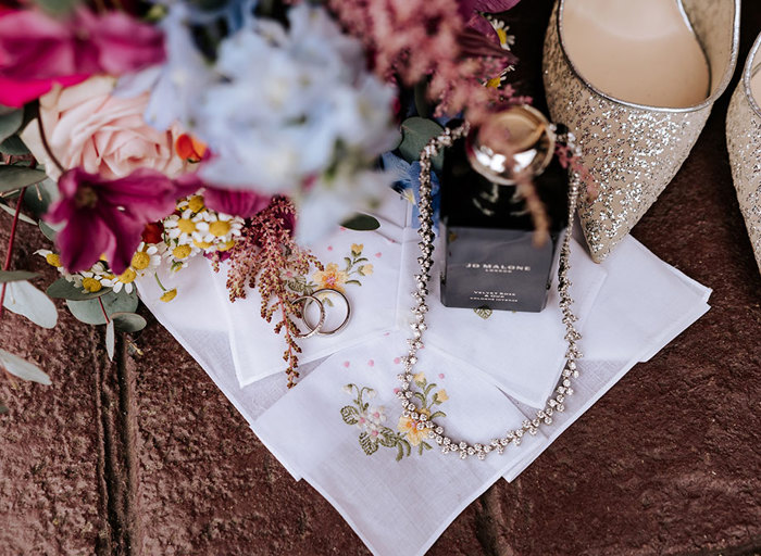 a styled image of perfume, necklace, shoes and flowers