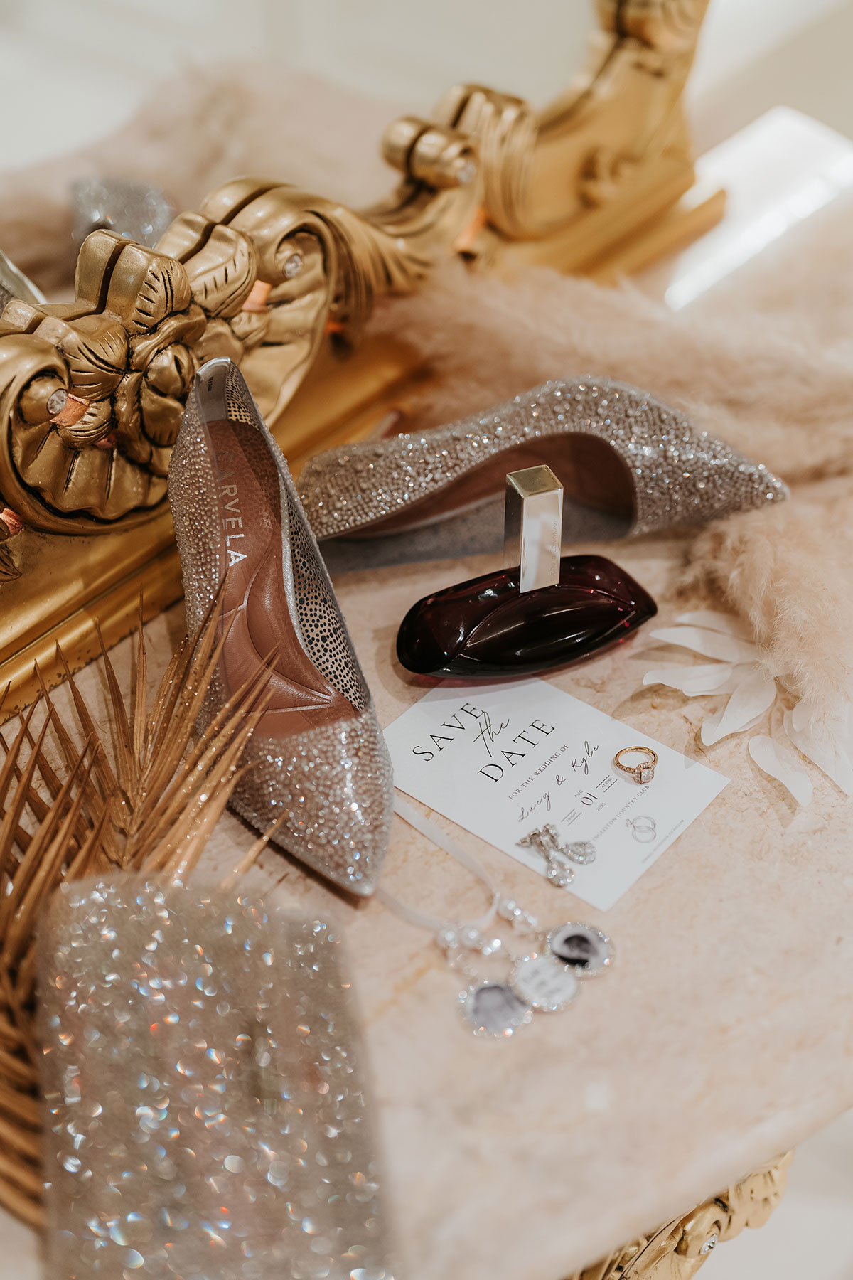 Bridal details with glitter wedding shoes, perfume, jewellery and save the date card styled on marble table at Ingliston Country Club