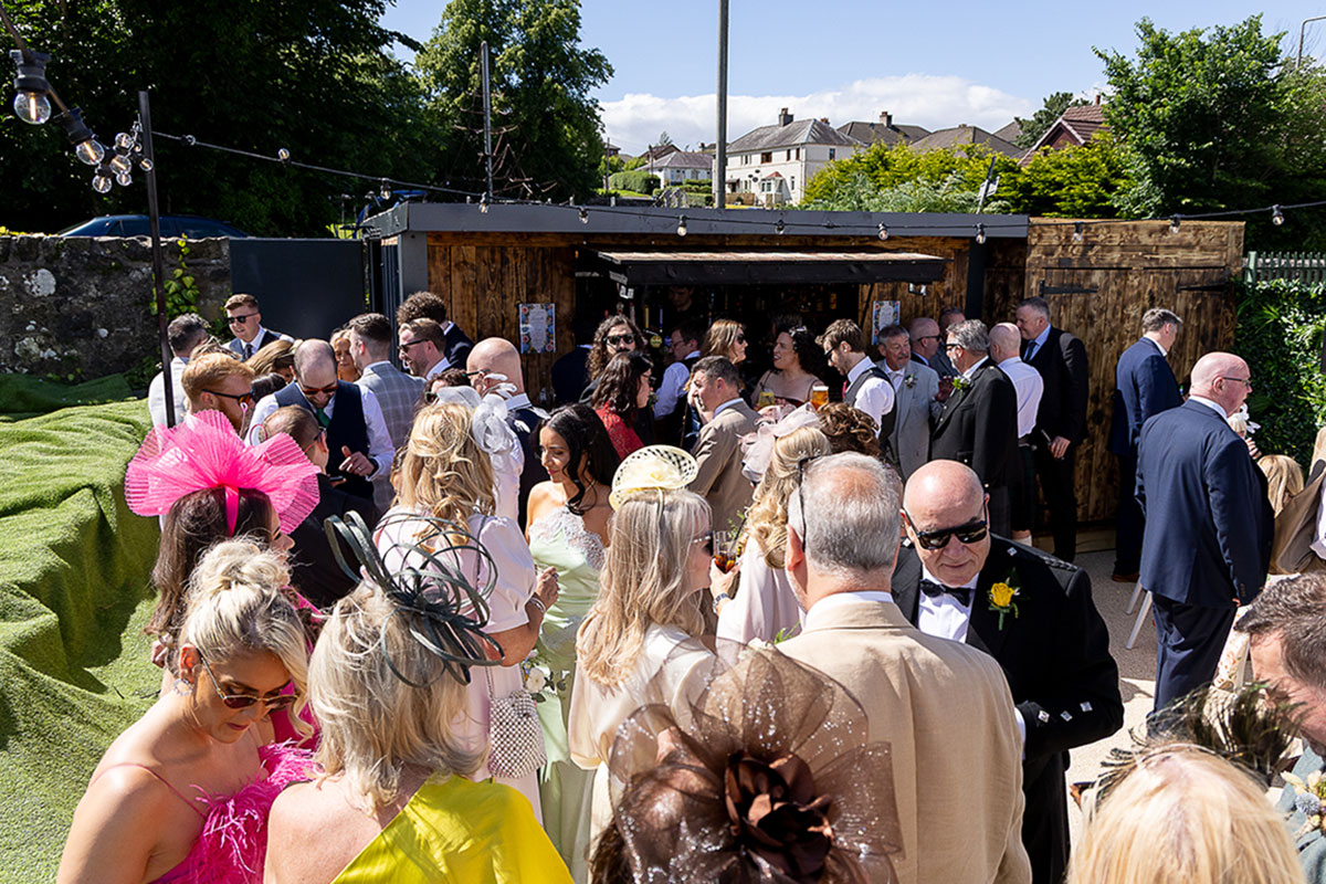 Wedding guests enjoying an outdoor drinks reception beside the garden bar at The River Inn in Renfrewshire.