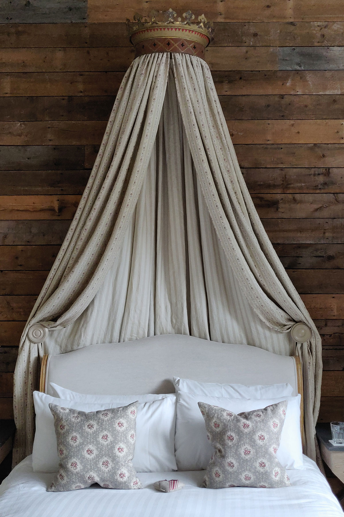 double bed with white linen bedding and floral cushions with draped curtains above it