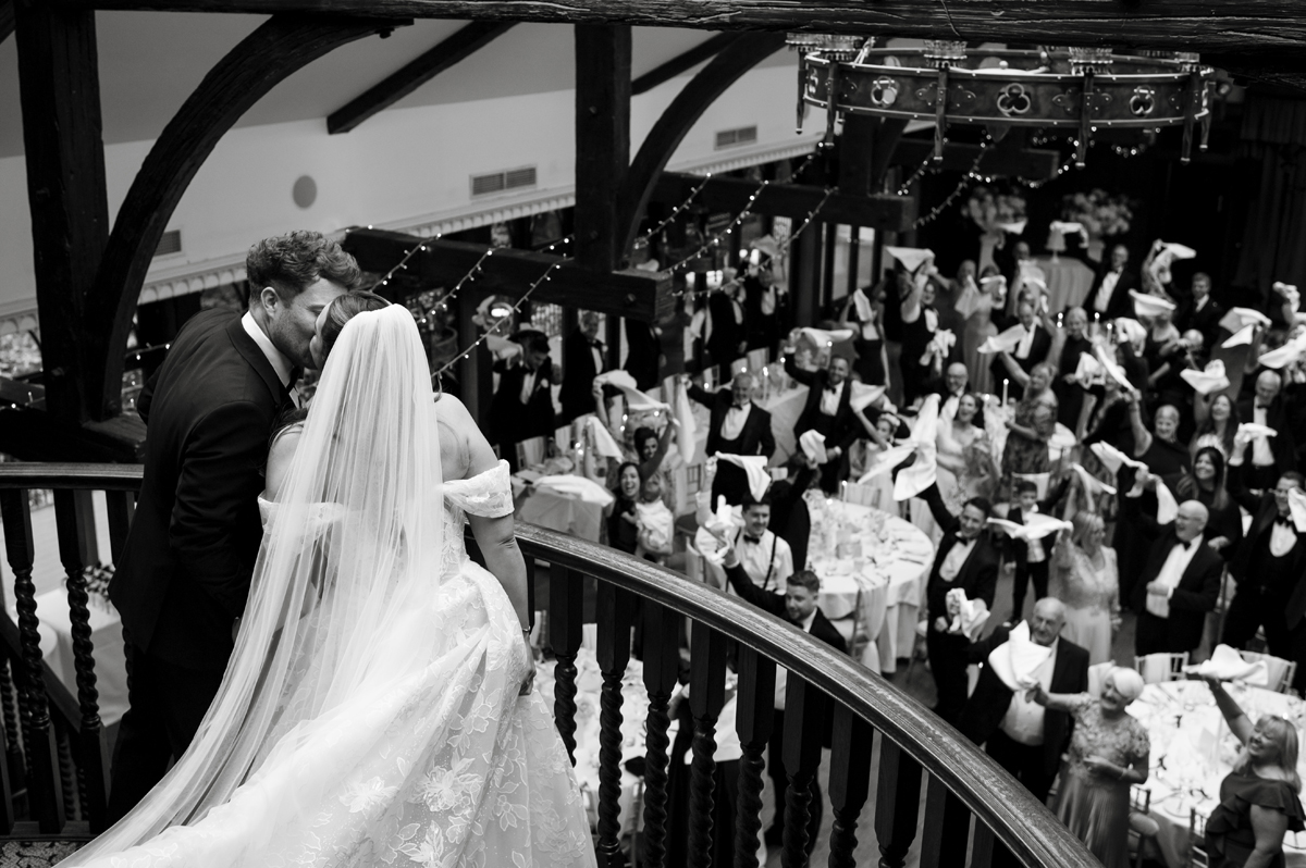 Bride and groom kissing on the balcony overlooking guests in the Roosevelt Ballroom at Crossbasket Castle.