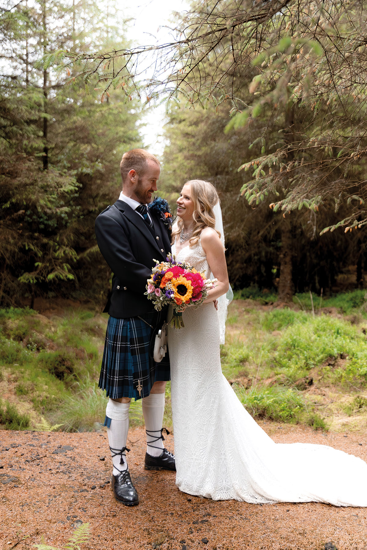 Bride and groom in Highland dress with a bright bouquet during a woodland wedding portrait at Eden Leisure Village near Glasgow