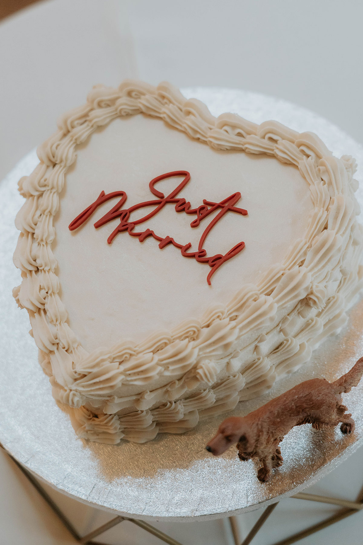 Heart-shaped vintage-style wedding cake with piped icing, red ‘Just Married’ lettering and a dog figurine