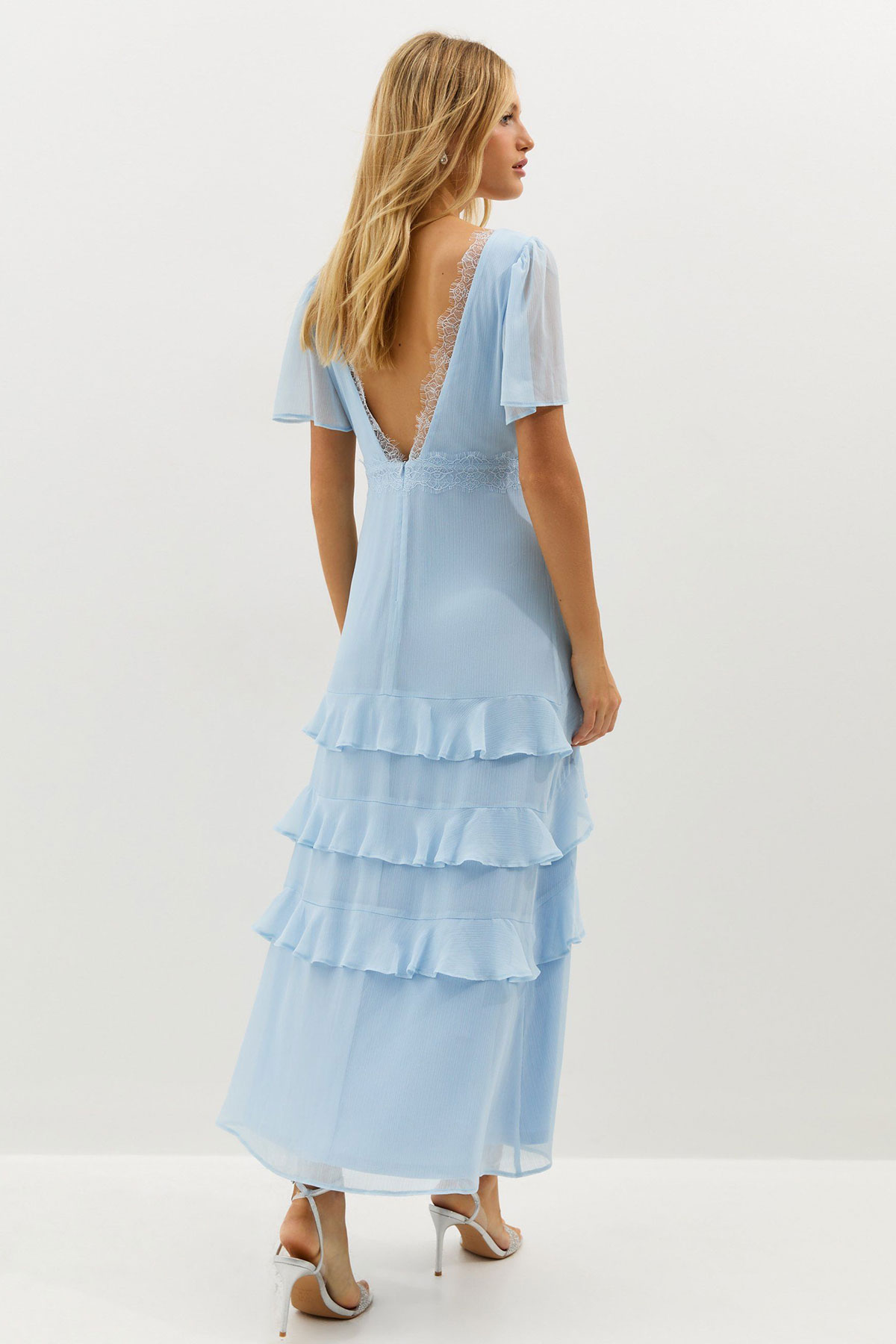 Light blue chiffon maxi dress with lace trim, flutter sleeves and tiered ruffle skirt styled in a studio setting
