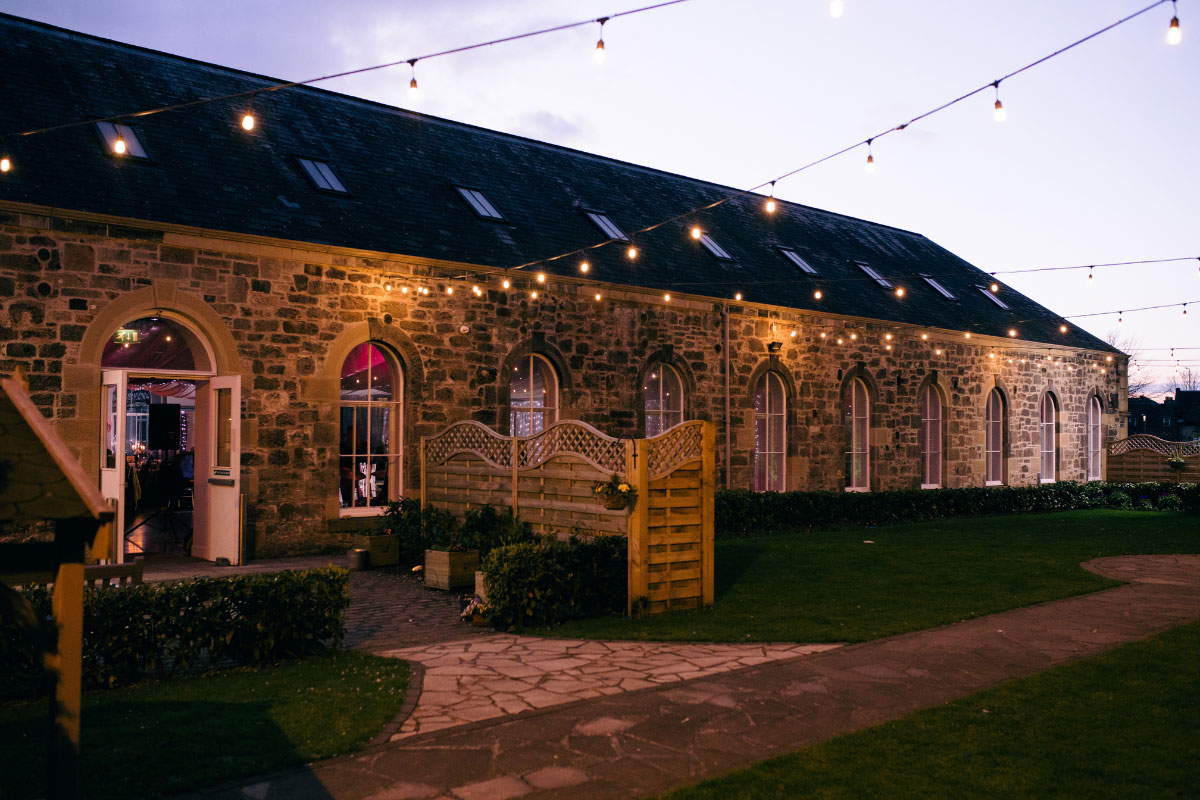 a stone barn in the evening with strings of fairylights draped off of the building
