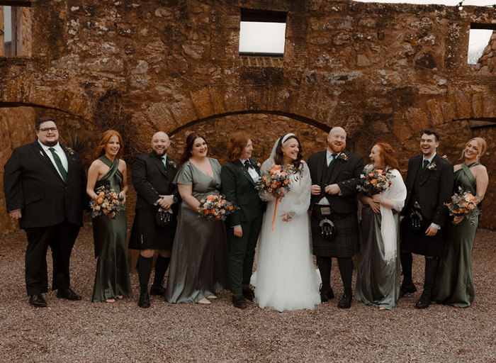 a line of people posing for a photo at a wedding at Cow Shed Crail against a stone building with arches
