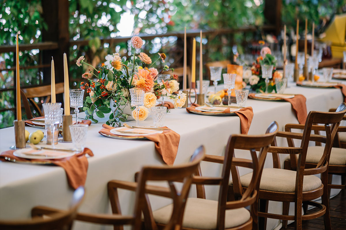 A long table with a white table cloth, orange napkins, orange flowers and orange candlesticks