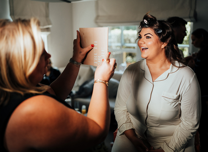 a woman with her hair in rollers smiling at her reflection in a small mirror being held up by another woman