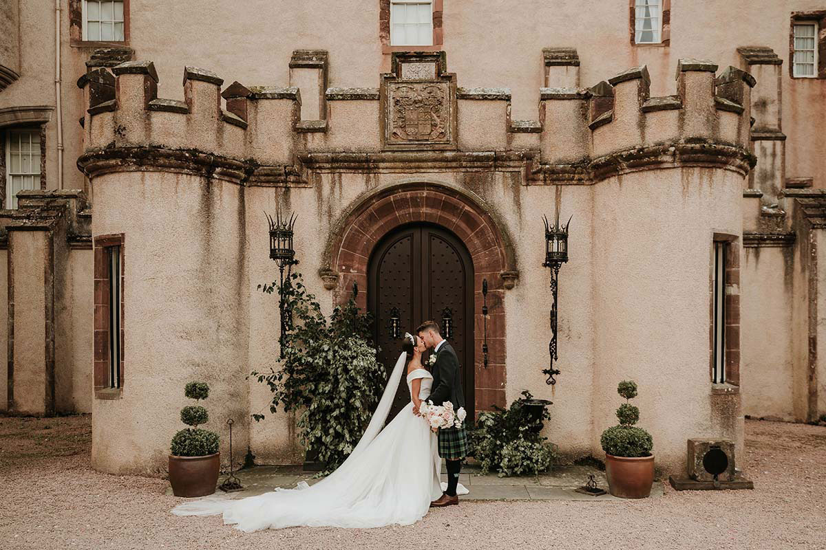 Bride and groom sharing a kiss outside a castle entrance with arched wooden doors and stone walls