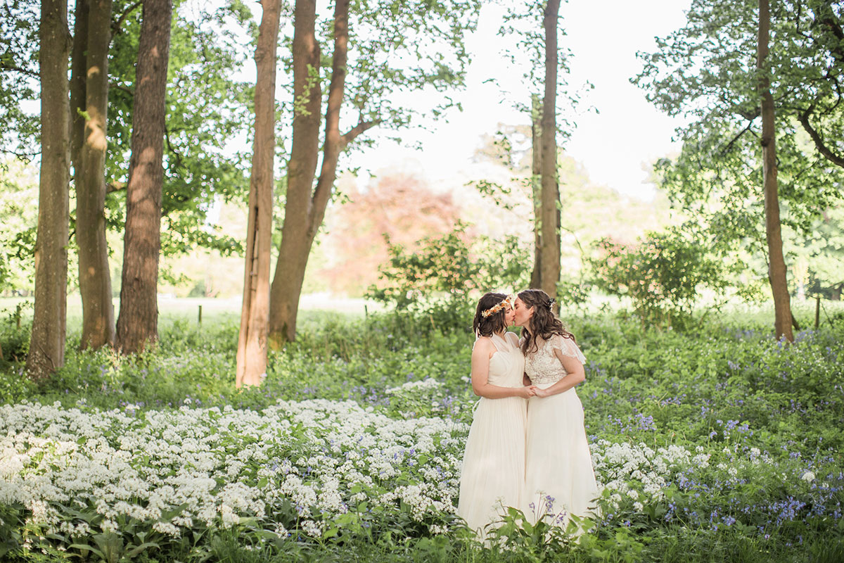 Two brides kissing in a forest setting with wildflowers