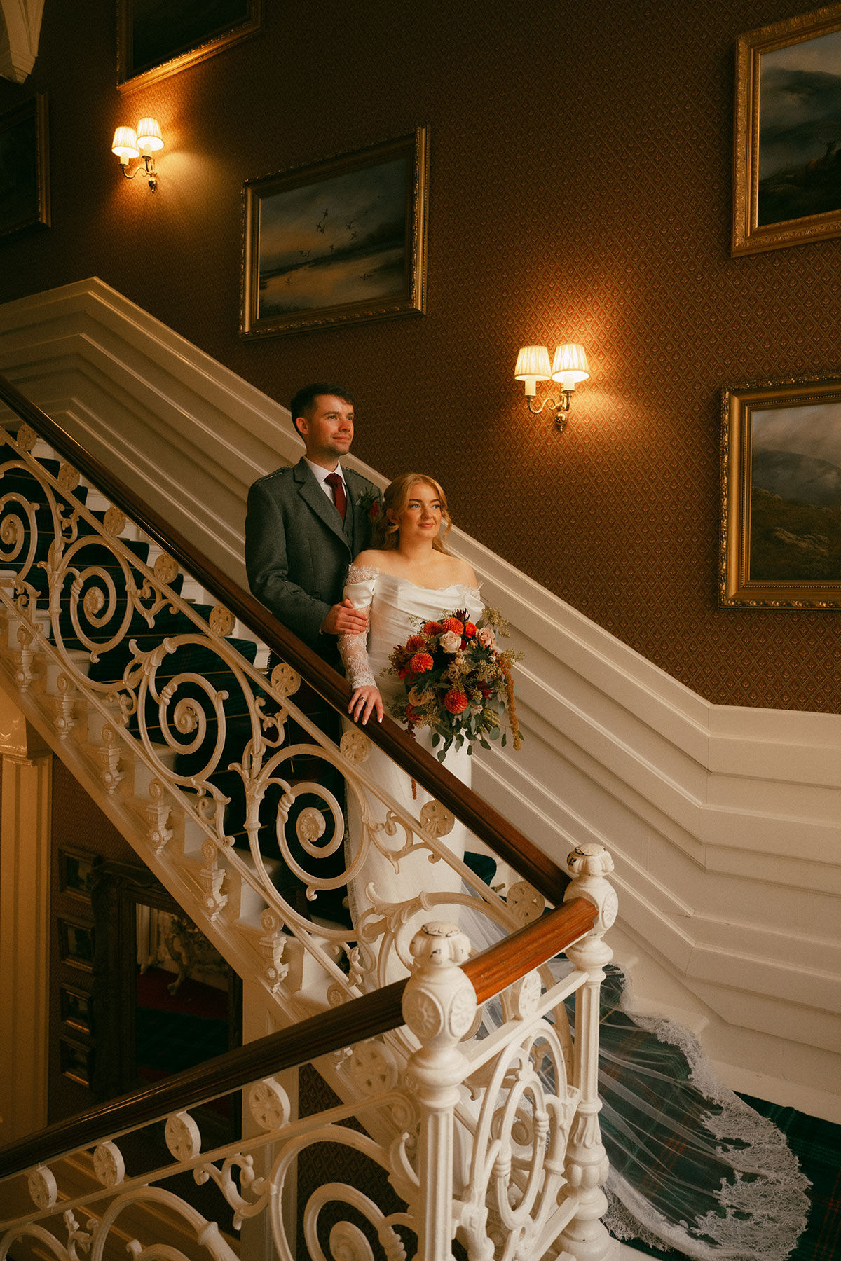 Bride and groom posing on grand staircase inside historic Scottish wedding venue with ornate details