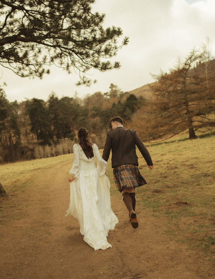 bride and groom hand in hand run into the woods with backs turned to the camera after eloping