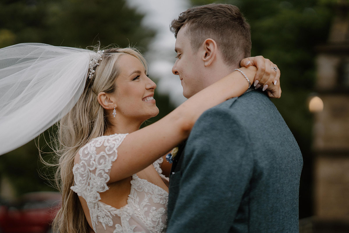 bride and groom smile at one another as bride's veil blows in the wind during wedding at cornhill castle