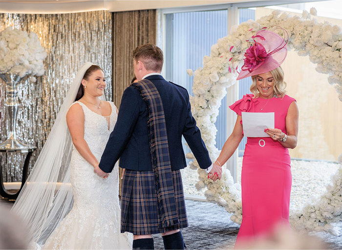 bride and groom standing at top of aisle with groom also holding hands with his mum 