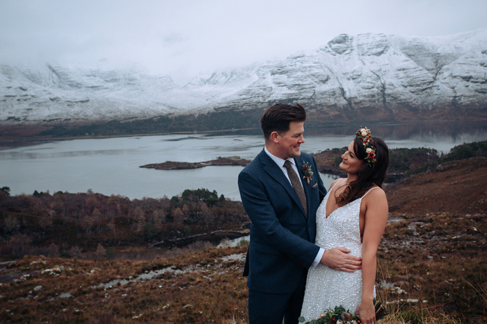 Bride and groom smile at each other in front of snow-capped mountain