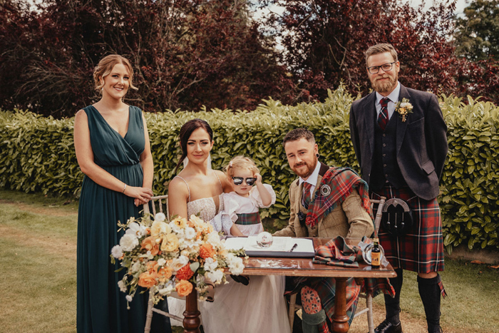 Couple sign register with bridesmaid and groomsman at their side and daughter on bride's lap