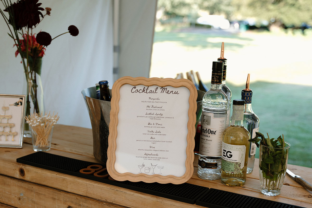 Wedding cocktail bar setup inside a marquee featuring a personalised cocktail menu, spirits and fresh garnishes at a Scottish outdoor wedding