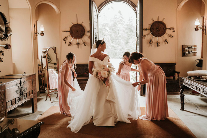 Three bridesmaids in pink dresses adjust the train of a bride's dress