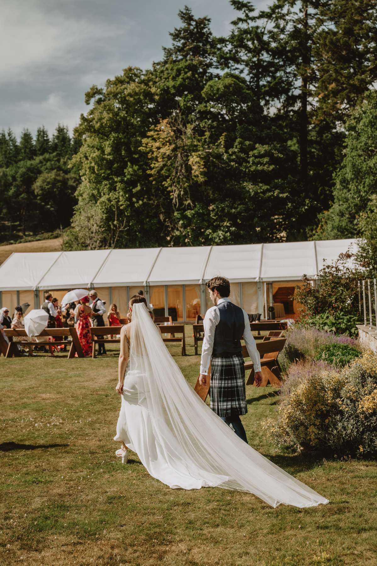 Bride and groom walk across the lawn towards the wedding marquee at Ballogie House