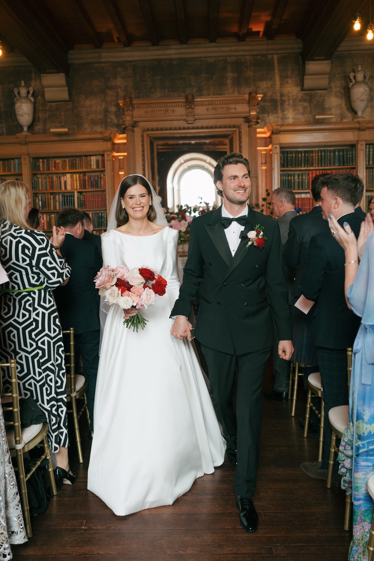Newlyweds Nicole and Ryan walk hand in hand down the aisle as guests applaud following their Barnbougle Castle library wedding ceremony.