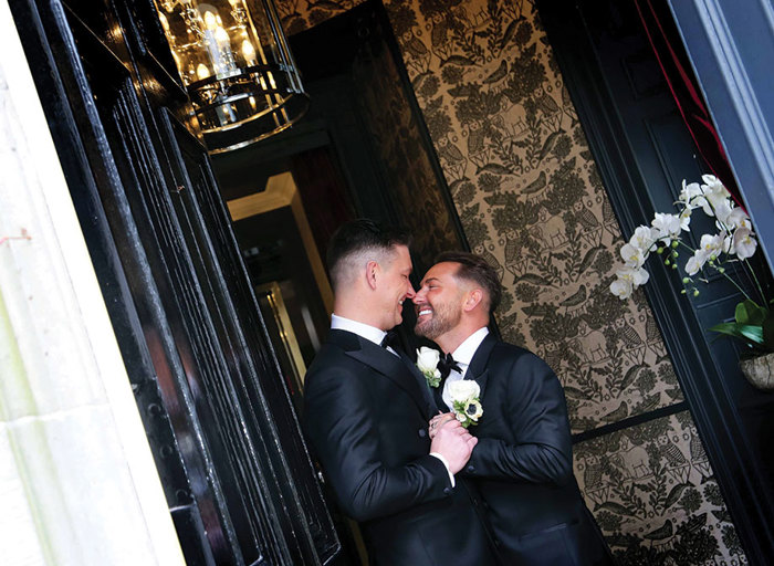 two smiling grooms stand nose to nose in a doorway at Carlowrie Castle