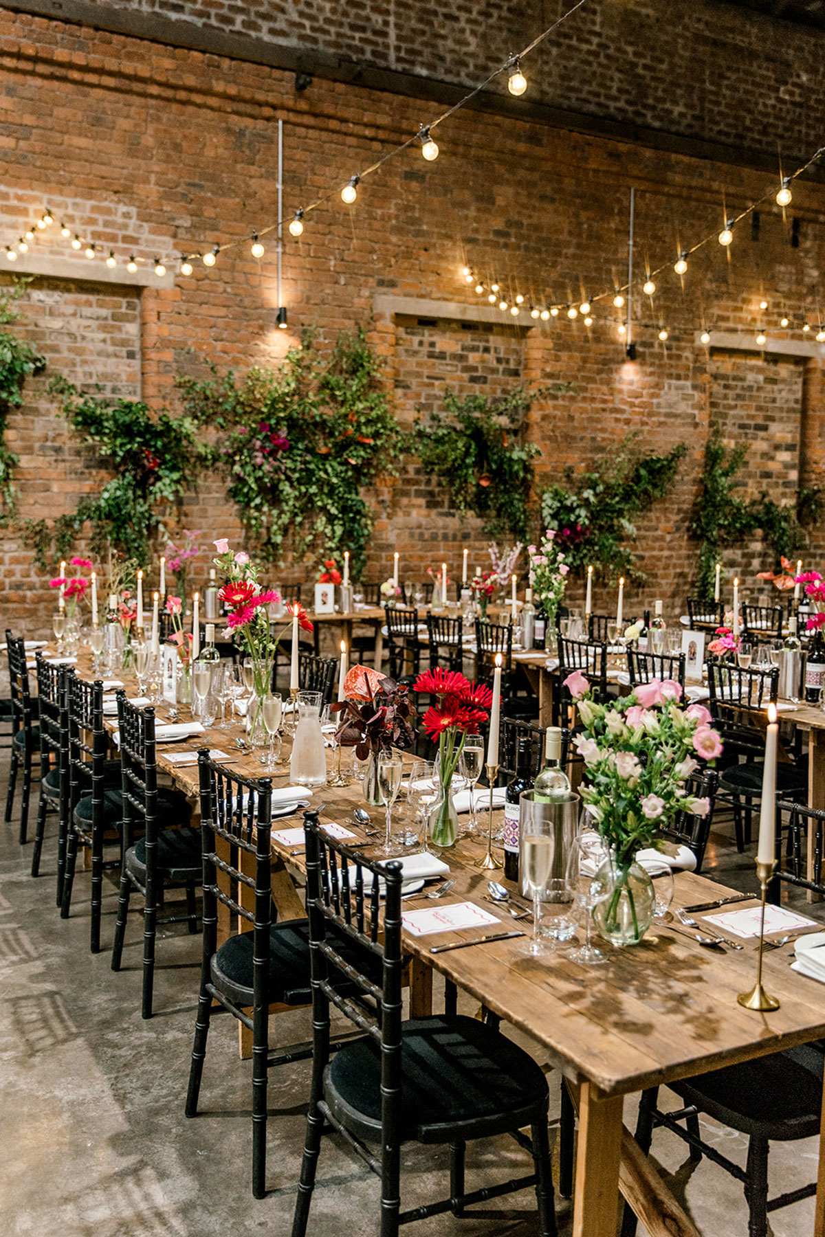 Long wooden banquet tables styled with colourful flowers, candles and glassware in an industrial venue