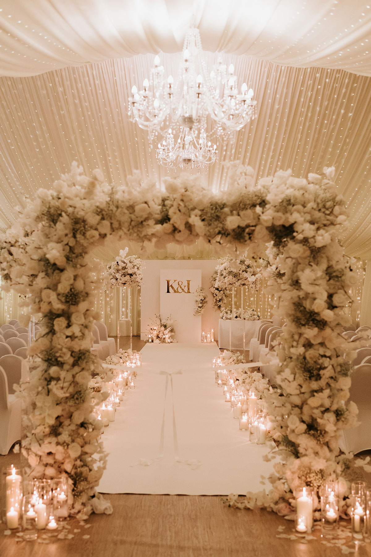 Ingliston Country Club wedding ceremony setup with floral arch, candlelit aisle and chandelier in marquee