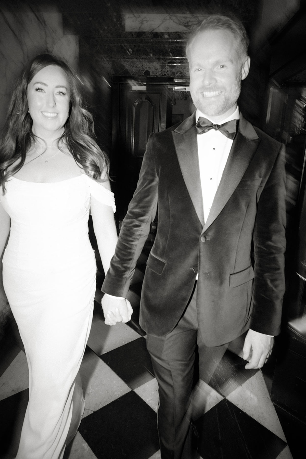a smiling bride and groom walking hand-in-hand across a black and white checked floor at the Scotsman Hotel