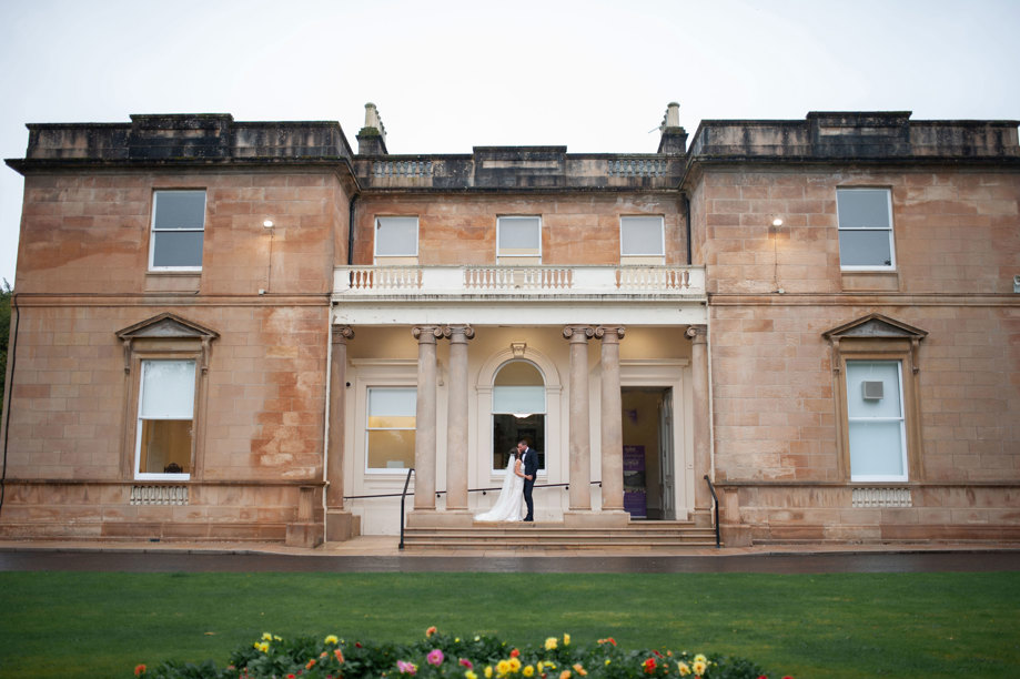 exterior of kilmardinny house with bride and groom kissing in front