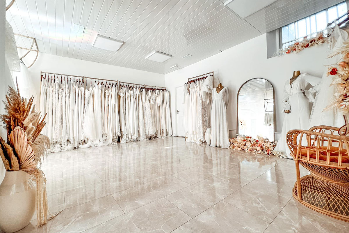 inside view of a bridal boutique where wedding dresses are hanging on a rail along wall and there's a lot of open space showing the marble floors