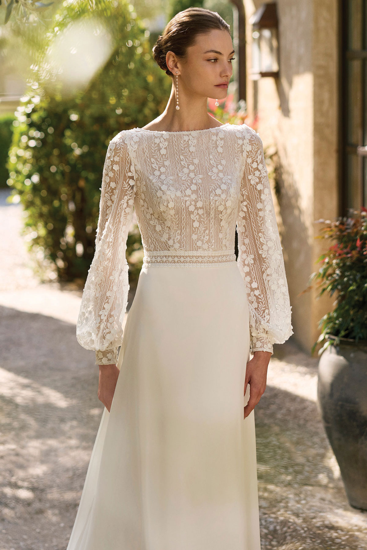 Model wearing an ivory wedding dress with a floral lace bodice, long sleeves and flowing skirt.