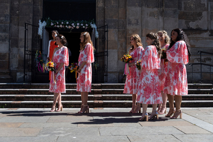 Bridesmaids wearing pink and orange floral dresses stand outside St Luke's in Glasgow