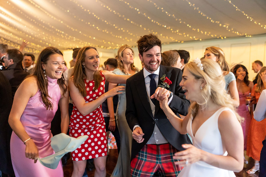 Bride and groom smile with friends on the dance floor