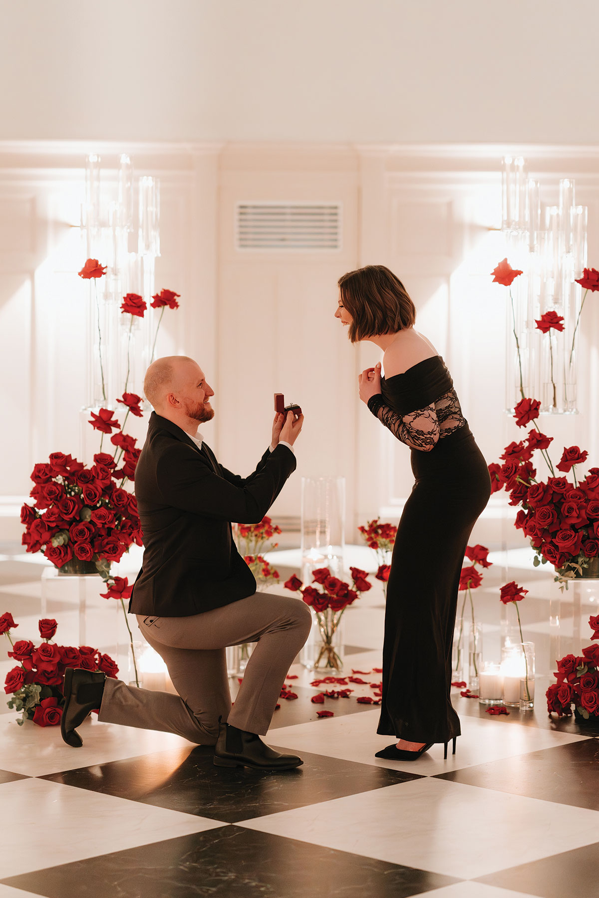 Romantic proposal moment with red rose styling, candles and black-and-white chequered floor