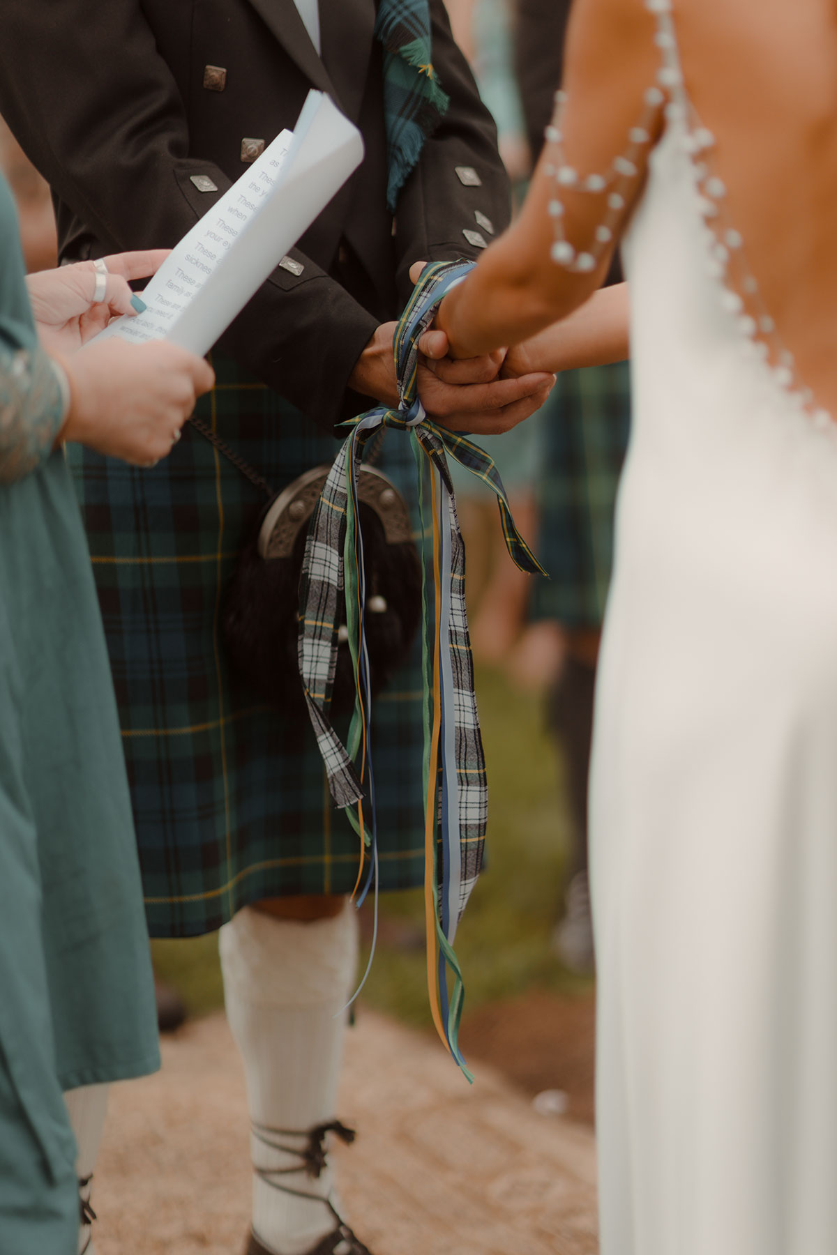 a close up of a bride and groom handfasting with tartan ribbons
