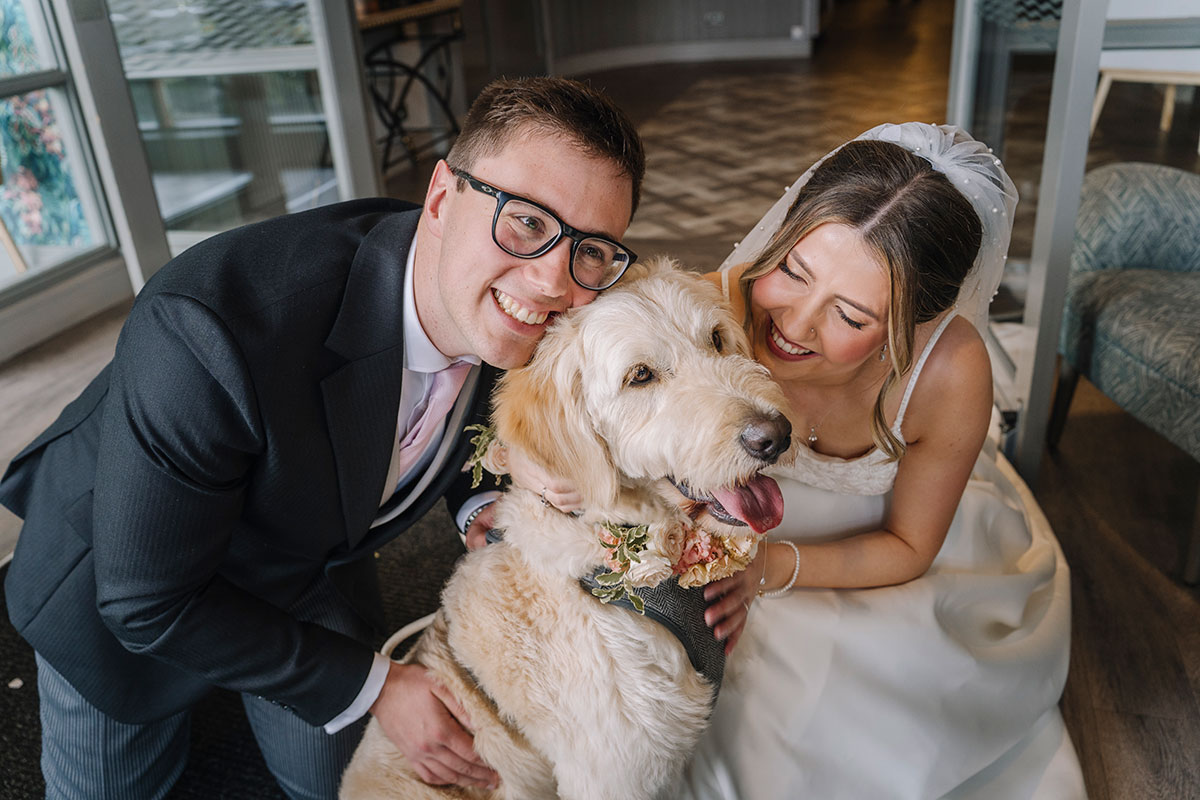 Bride and groom smiling with their dog wearing a floral collar during their wedding day at Gailes Hotel & Spa